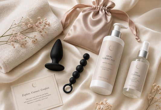 Beginner anal play essentials arranged in a luxury flat-lay with anal plug, anal beads, lubricant, toy cleaner and satin pouch.