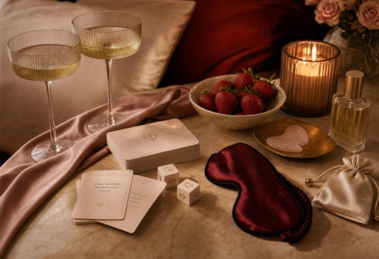 Luxury flat-lay of couples card game, dice, blindfold, candle, champagne glasses and romantic date-night essentials.