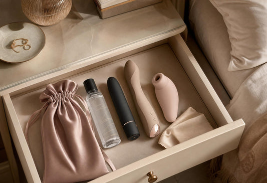 Luxury flat-lay of quiet intimate wellness products including bullet vibrator, palm vibrator, lubricant and satin pouch for discreet pleasure.