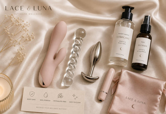 Body-safe intimate wellness products arranged in a luxury flat-lay with silicone, glass, stainless steel, lubricant and toy cleaner.