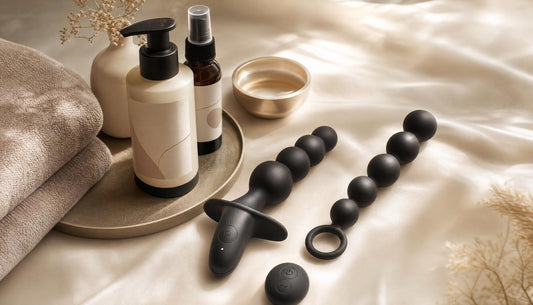 Vibrating anal beads and classic anal beads compared in a luxury flat-lay with anal lubricant, toy cleaner, satin pouch and discreet wellness essentials.