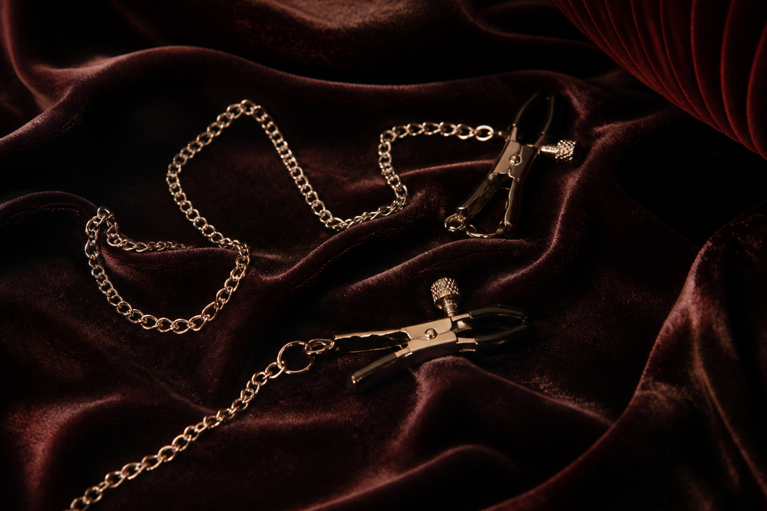 ilver nipple clamps on charcoal velvet with warm amber lighting
