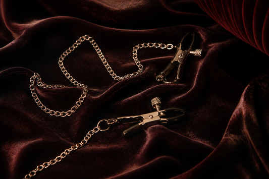ilver nipple clamps on charcoal velvet with warm amber lighting
