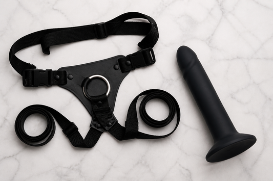 Flat lay of strap-on harness with O-ring and body-safe silicone dildo with flared base on marble